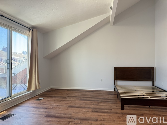 A bedroom with a bed, wooden floors, and a window with a view of buildings outside.