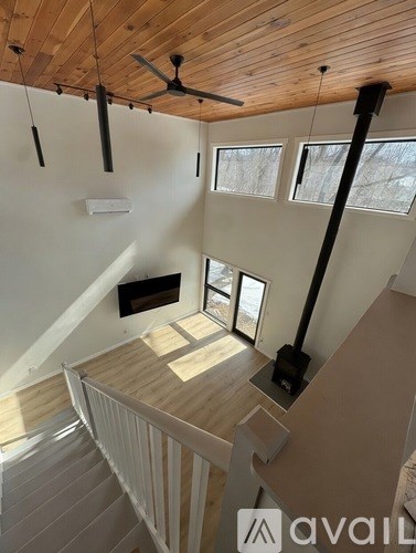 A wooden staircase with a white railing leads to a room with a ceiling fan and three windows.