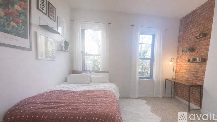 A bedroom with a red bedspread and a brick wall.