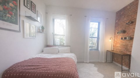 A bedroom with a red bedspread and a brick wall.