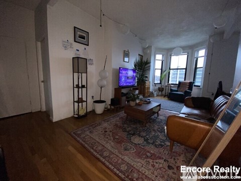 A living room with a rug, a couch, a chair, a table, a TV, and a plant.
