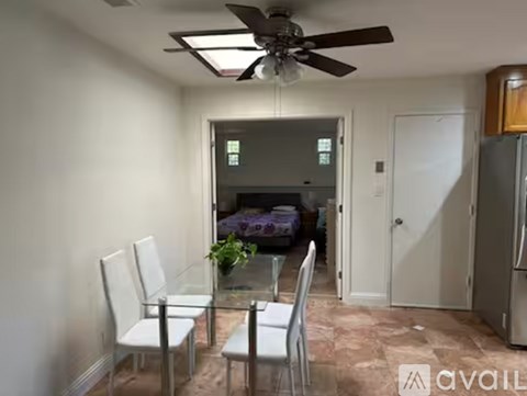 A living room with a glass table and chairs, a ceiling fan, and a door leading to a bedroom.
