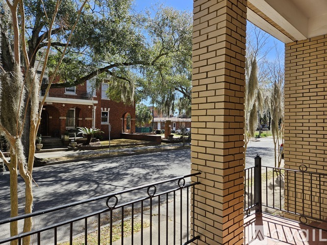 A view from a balcony looking out at a street with a brick building and trees.