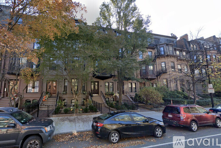 A row of brown houses with cars parked in front.