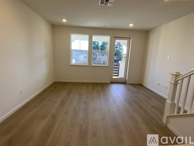 A spacious room with wooden flooring and a staircase on the right side.