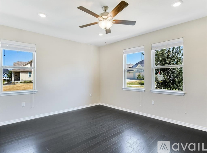 A spacious room with a ceiling fan and two windows showing outdoor views.