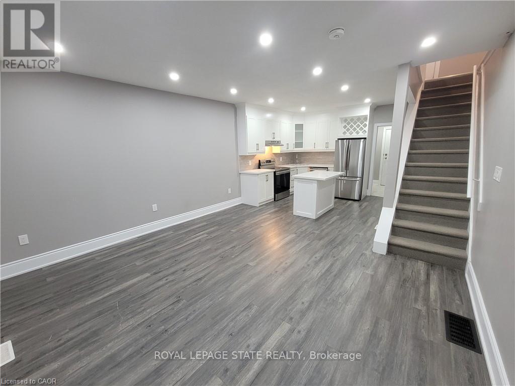 A spacious room with wooden flooring and a staircase leading to another room.