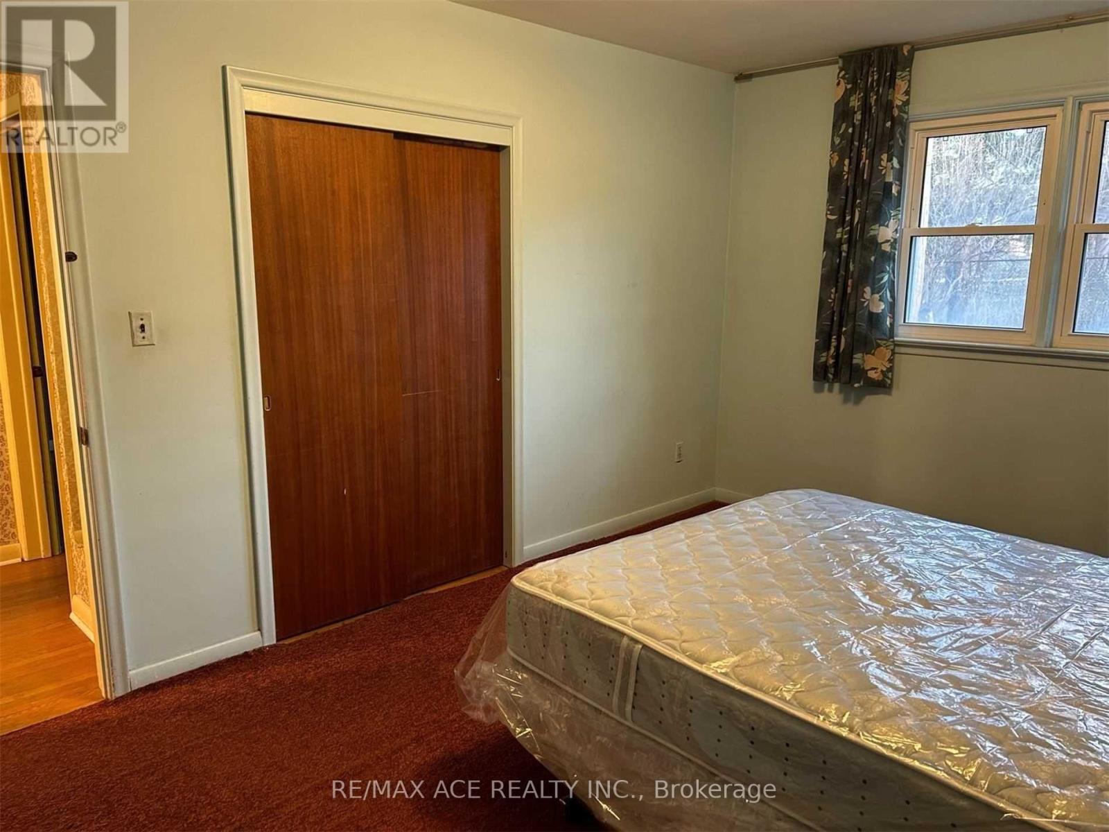 A bedroom with a bed covered in plastic, a door, and a window with curtains.