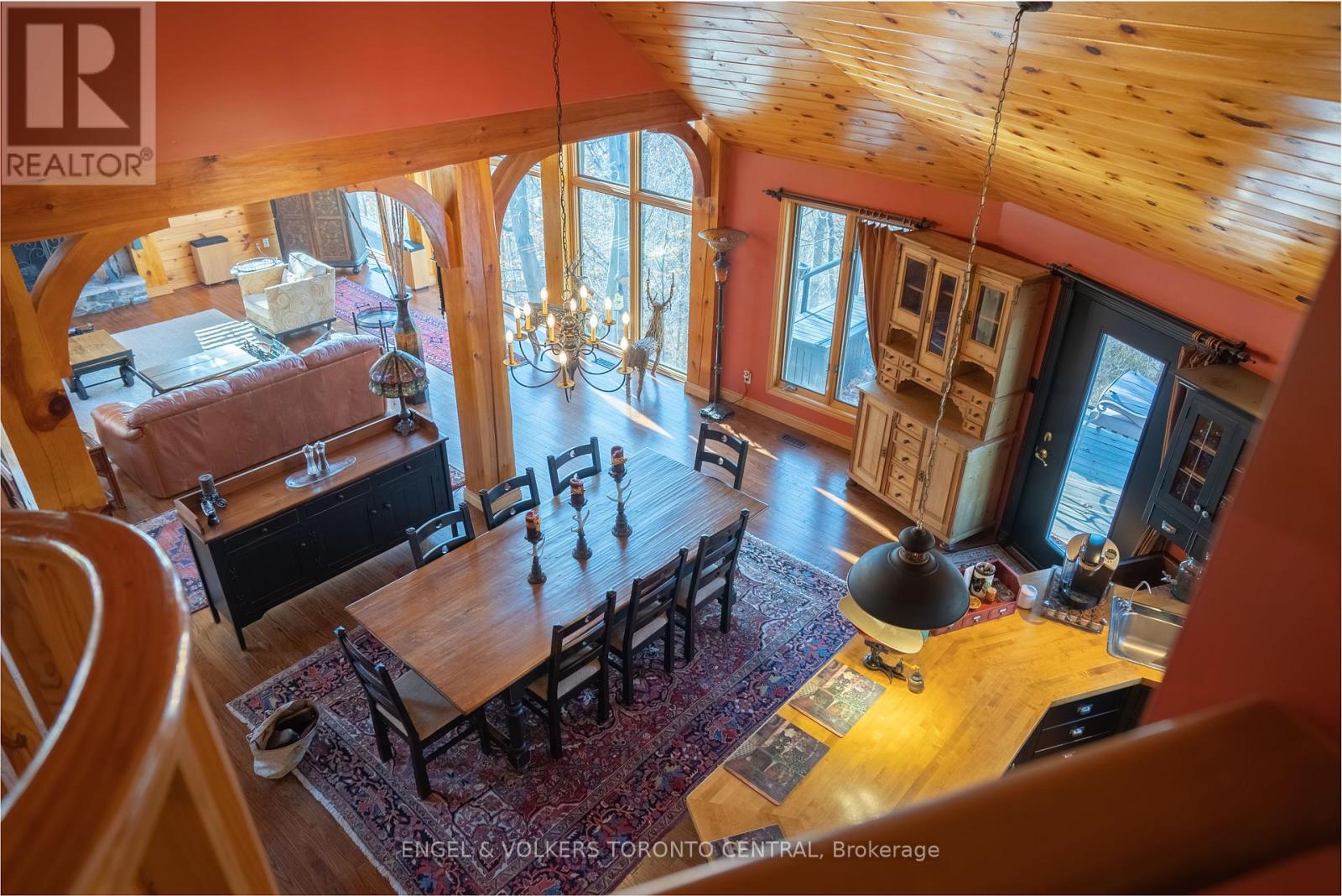 A large wooden dining table with chairs is in the center of a spacious room with a chandelier hanging from the ceiling.
