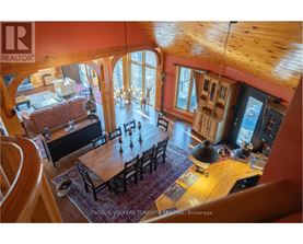 A large wooden dining table with chairs is in the center of a spacious room with a chandelier hanging from the ceiling.