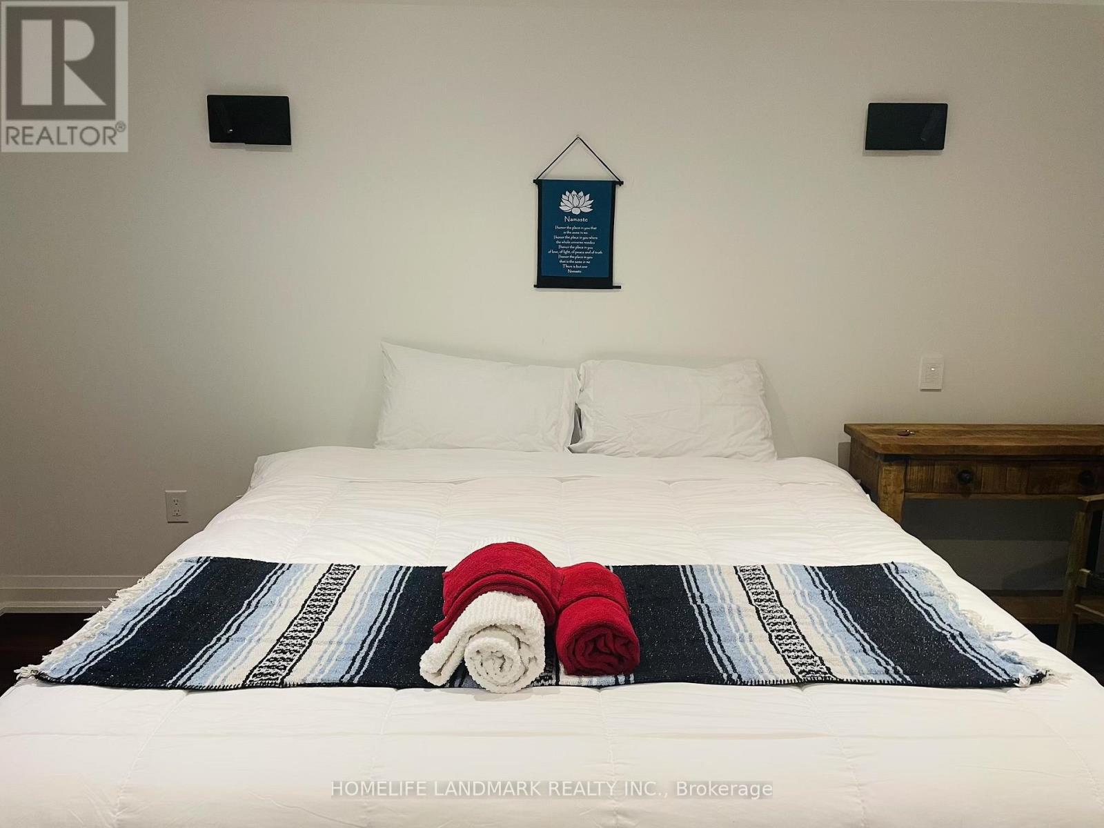 A bed with a white sheet and a blue and white striped blanket with a red and white striped pillow on it.