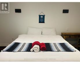 A bed with a white sheet and a blue and white striped blanket with a red and white striped pillow on it.