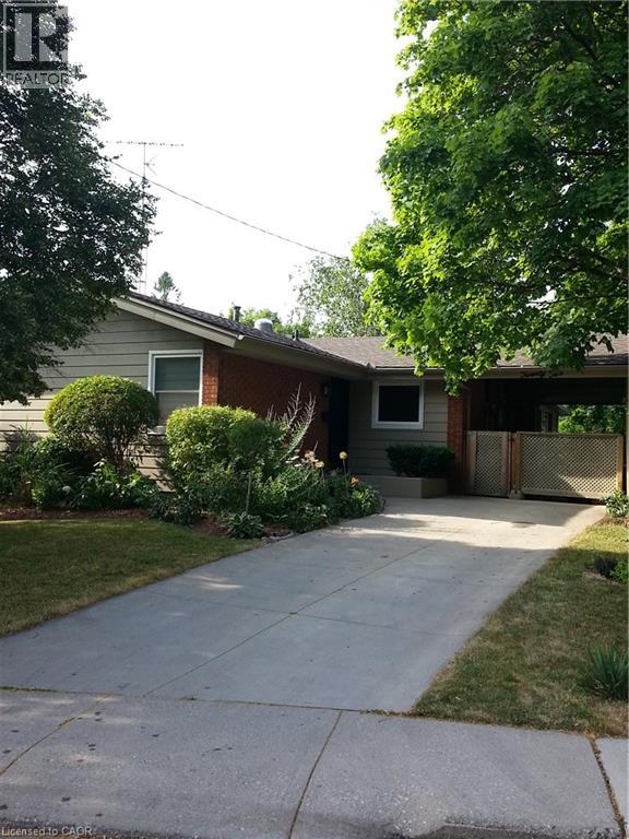 A house with a brown roof and a grey wall is surrounded by greenery.