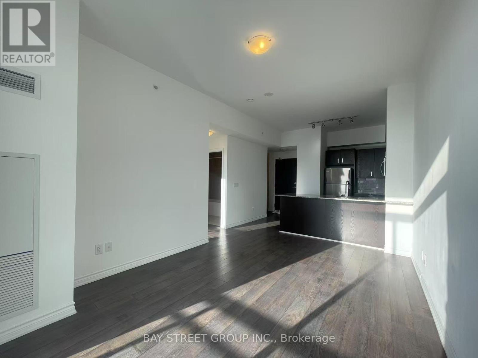 A spacious room with wooden floors and white walls, with a bay window on the left.