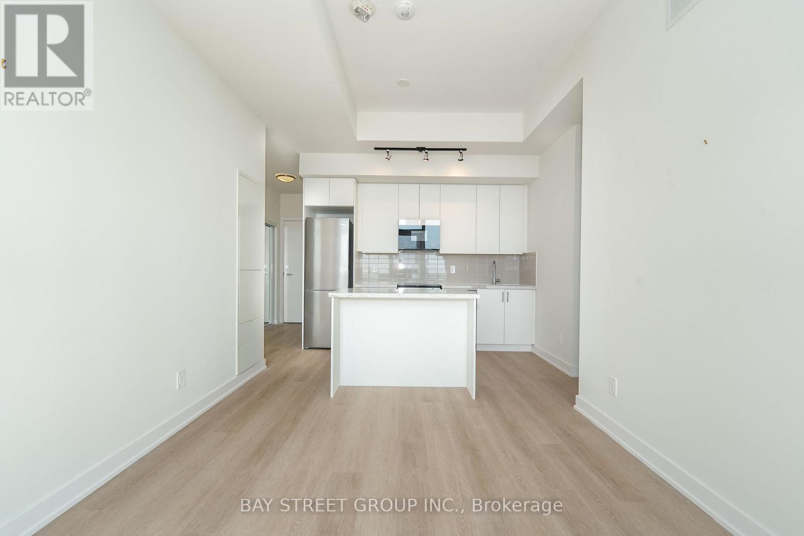 A white kitchen with a white island in the middle of a white hallway.