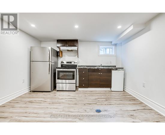 A kitchen with a refrigerator, oven, and dishwasher in a room with wooden flooring.