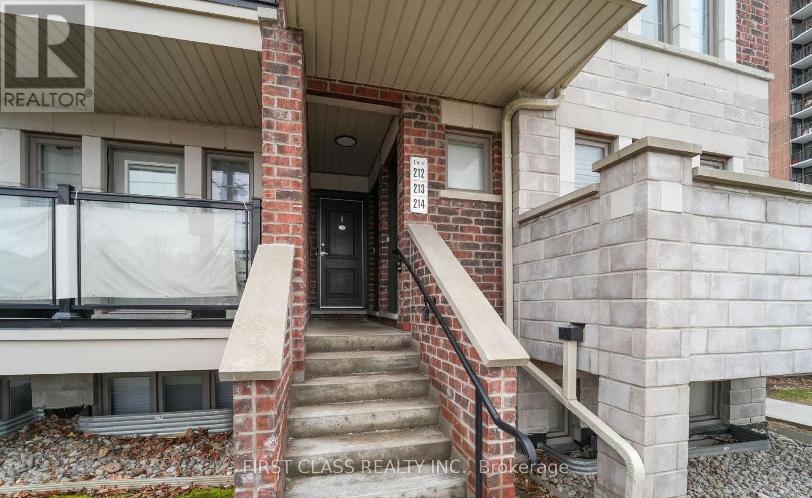 A brick house with a black door and a balcony with a glass railing.