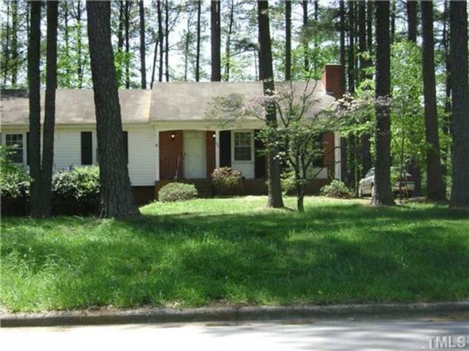 A house with a red door is surrounded by trees.