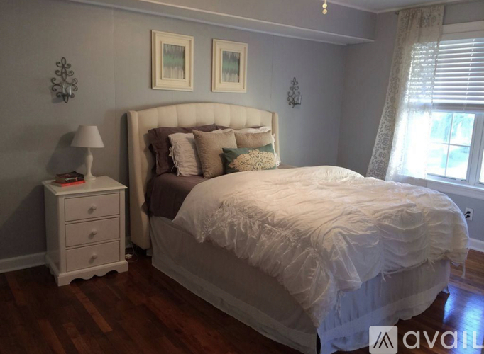 A bedroom with a large bed, a nightstand, and two framed pictures on the wall.