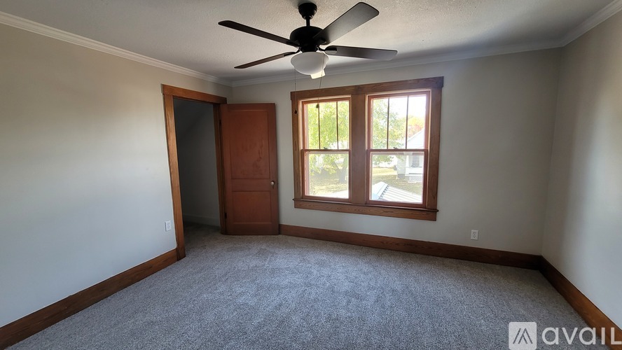 A room with a ceiling fan and a window with a view of trees.