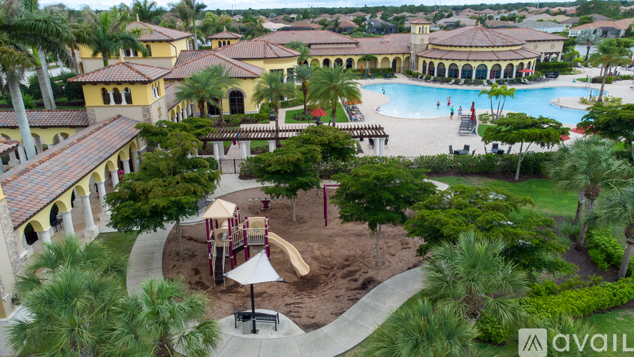 A playground with a slide and swings is surrounded by palm trees and a pool.