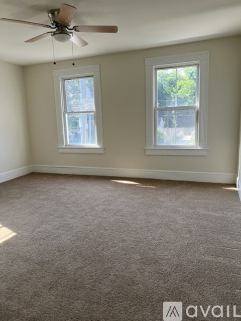 A room with a ceiling fan and two windows.
