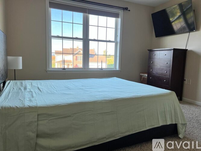 A bedroom with a bed, a dresser, and a window overlooking a building.