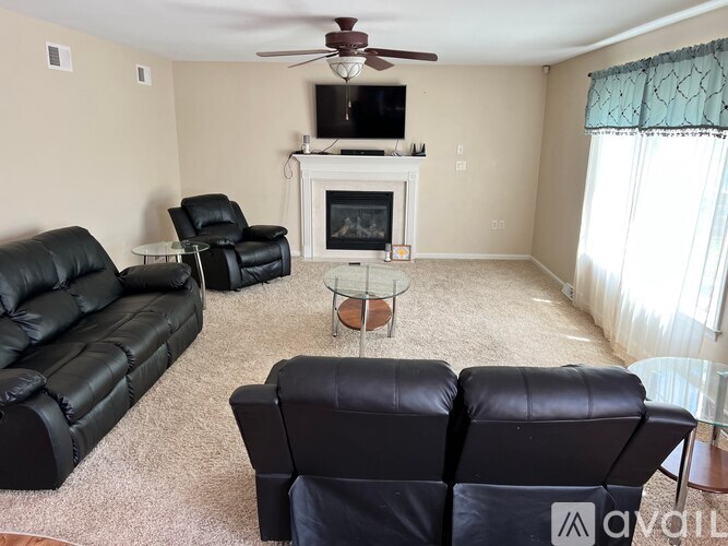 A living room with a fireplace, two black leather sofas, and a glass coffee table.