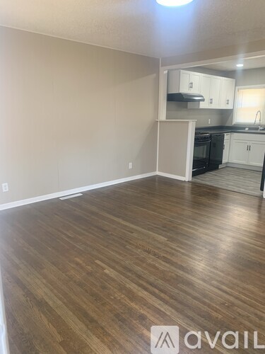 A room with wooden flooring and a kitchen area in the background.
