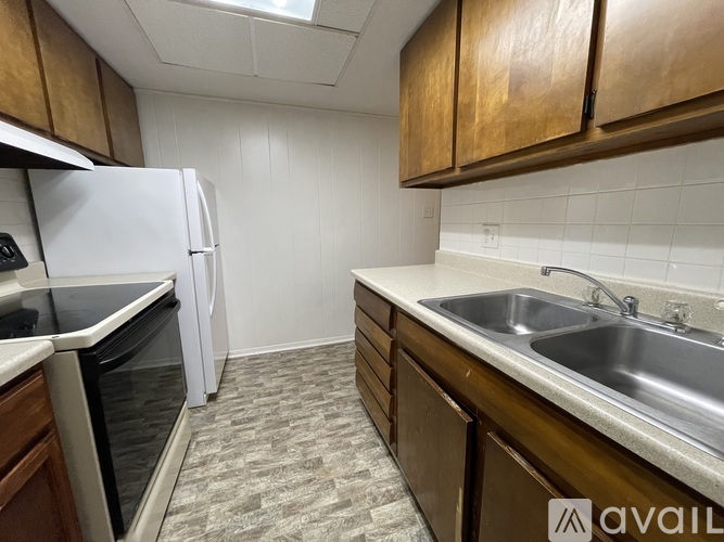 A kitchen with a white refrigerator, brown cabinets, and a stainless steel sink.