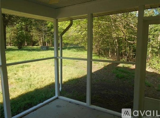 A white screened porch with a view of a grassy yard and trees.