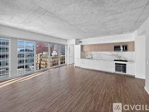 A spacious room with wooden flooring and a large window overlooking a cityscape.