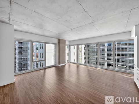 A spacious room with wooden floors and large windows overlooking a cityscape.