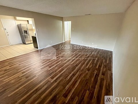 A spacious room with wooden flooring and a refrigerator in the corner.