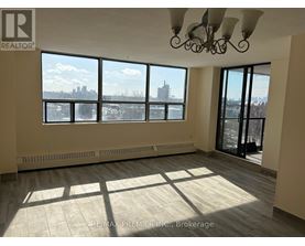 A large, empty room with a view of the city skyline through the windows.