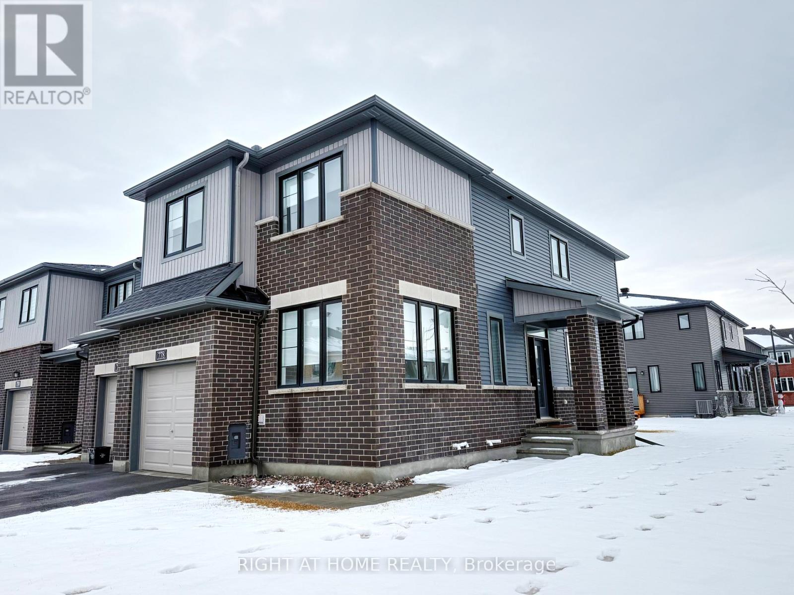 A house with a grey and brown exterior is surrounded by snow.