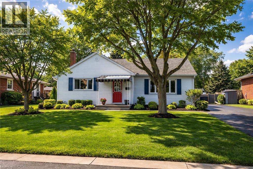 A white house with a red door and a tree in front.