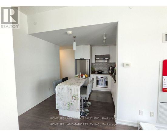 A kitchen area with a table and chairs in the foreground and a refrigerator in the background.