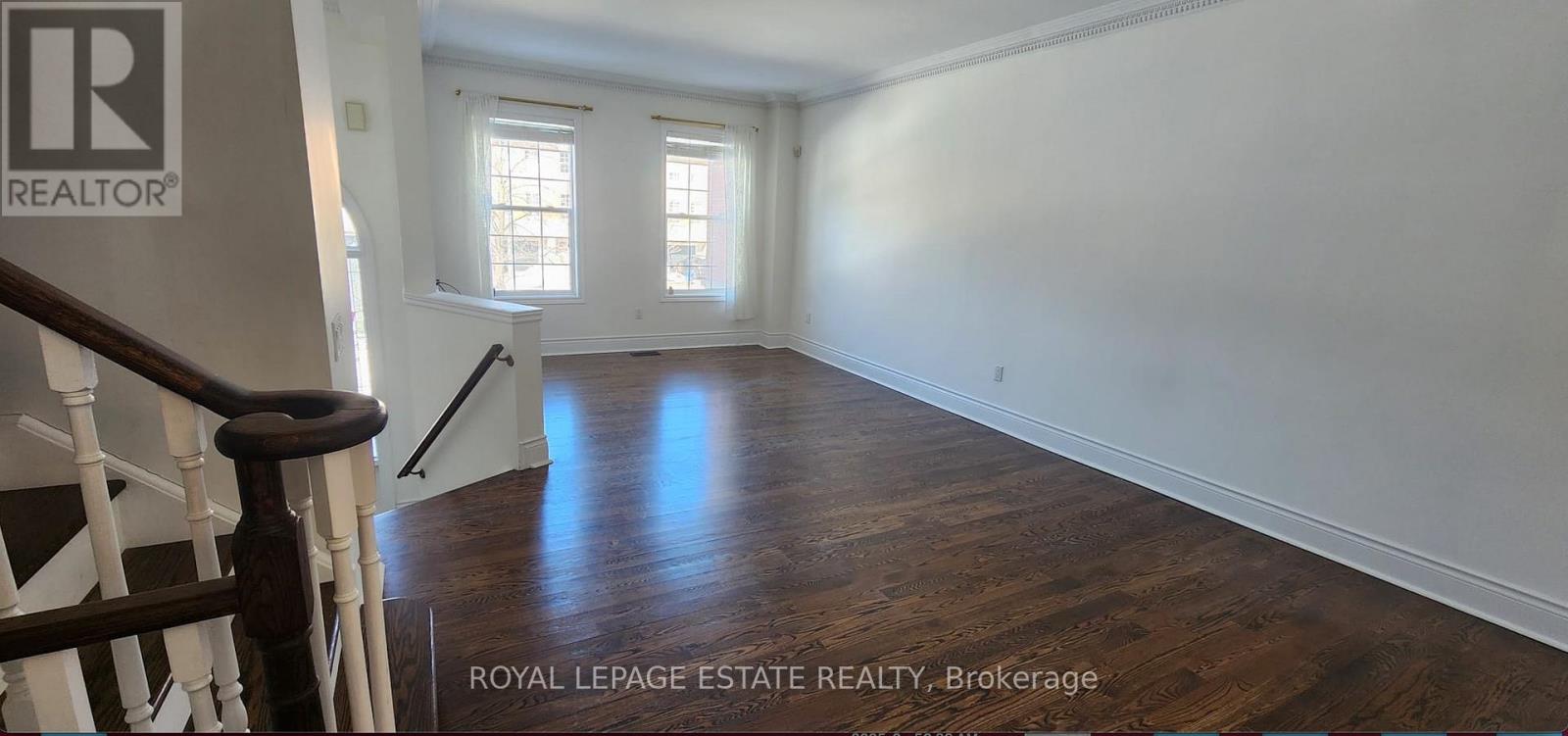 A spacious room with wooden floors and white walls, with a staircase on the left side.