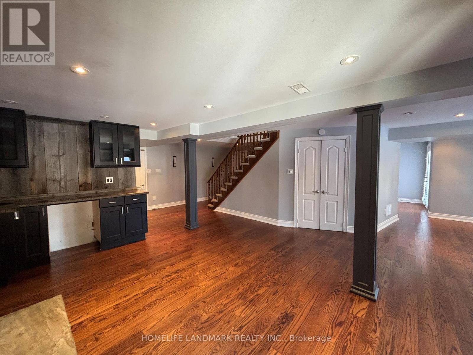 A spacious living room with wood flooring and a staircase in the background.