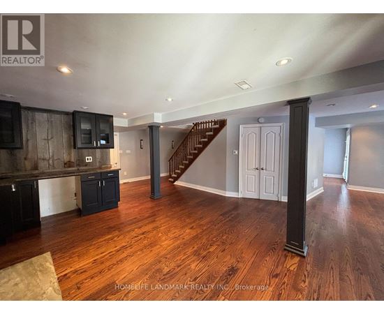 A spacious living room with wood flooring and a staircase in the background.