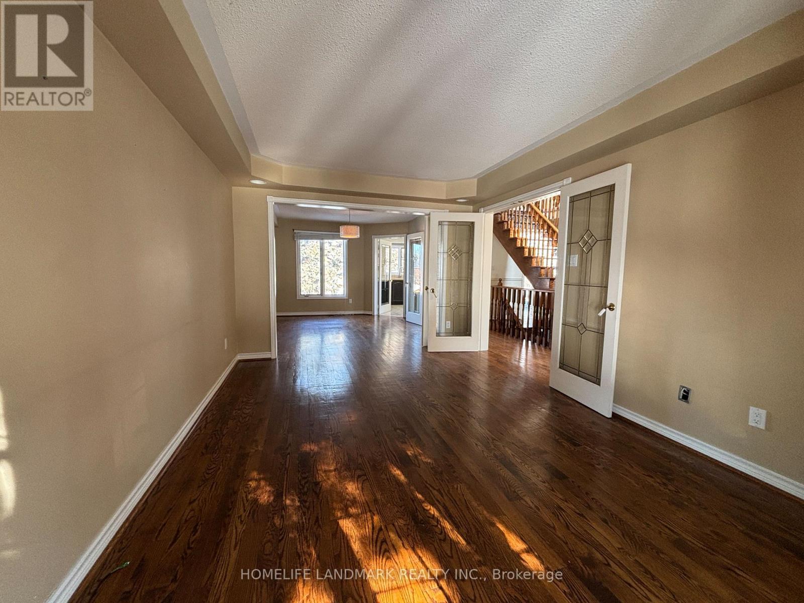 A spacious room with wooden floors and a staircase in the background.