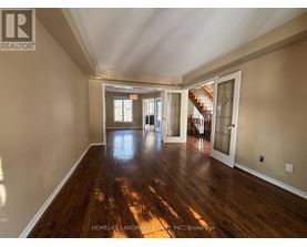 A spacious room with wooden floors and a staircase in the background.