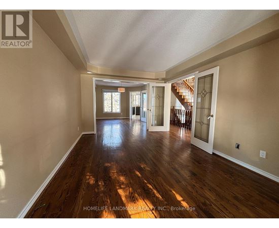 A spacious room with wooden floors and a staircase in the background.