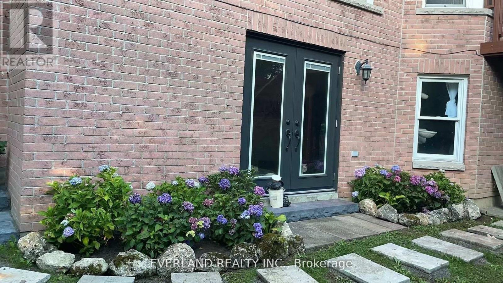 A brick house with a black door and a window with flowers in front.