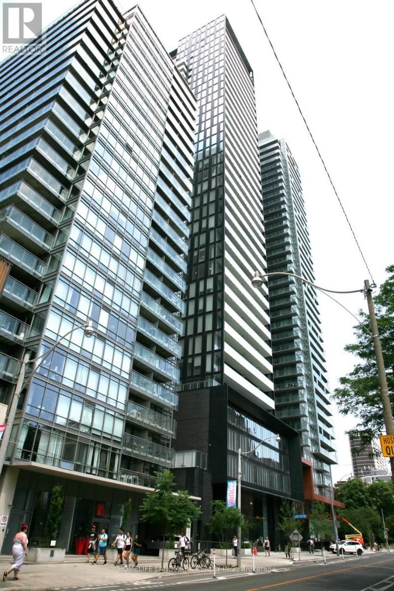 A tall building with a glass facade stands next to a street with people walking on the sidewalk.