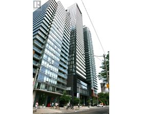 A tall building with a glass facade stands next to a street with people walking on the sidewalk.