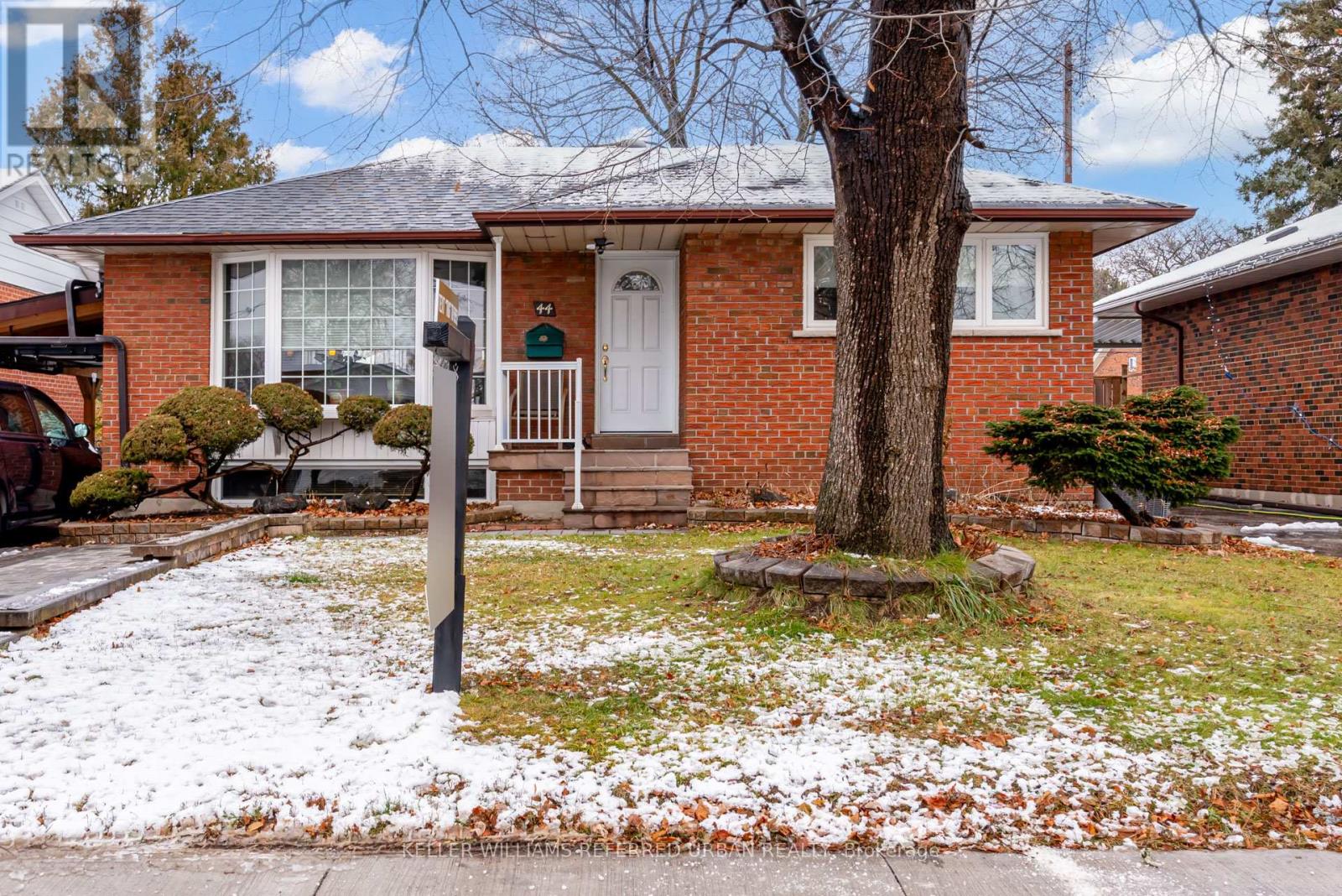 A red brick house with a white door and a tree in front.