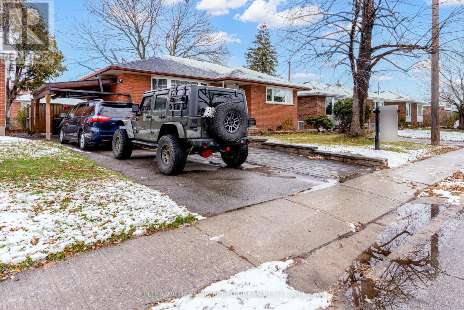 A black jeep is parked on a snowy sidewalk in front of a house.