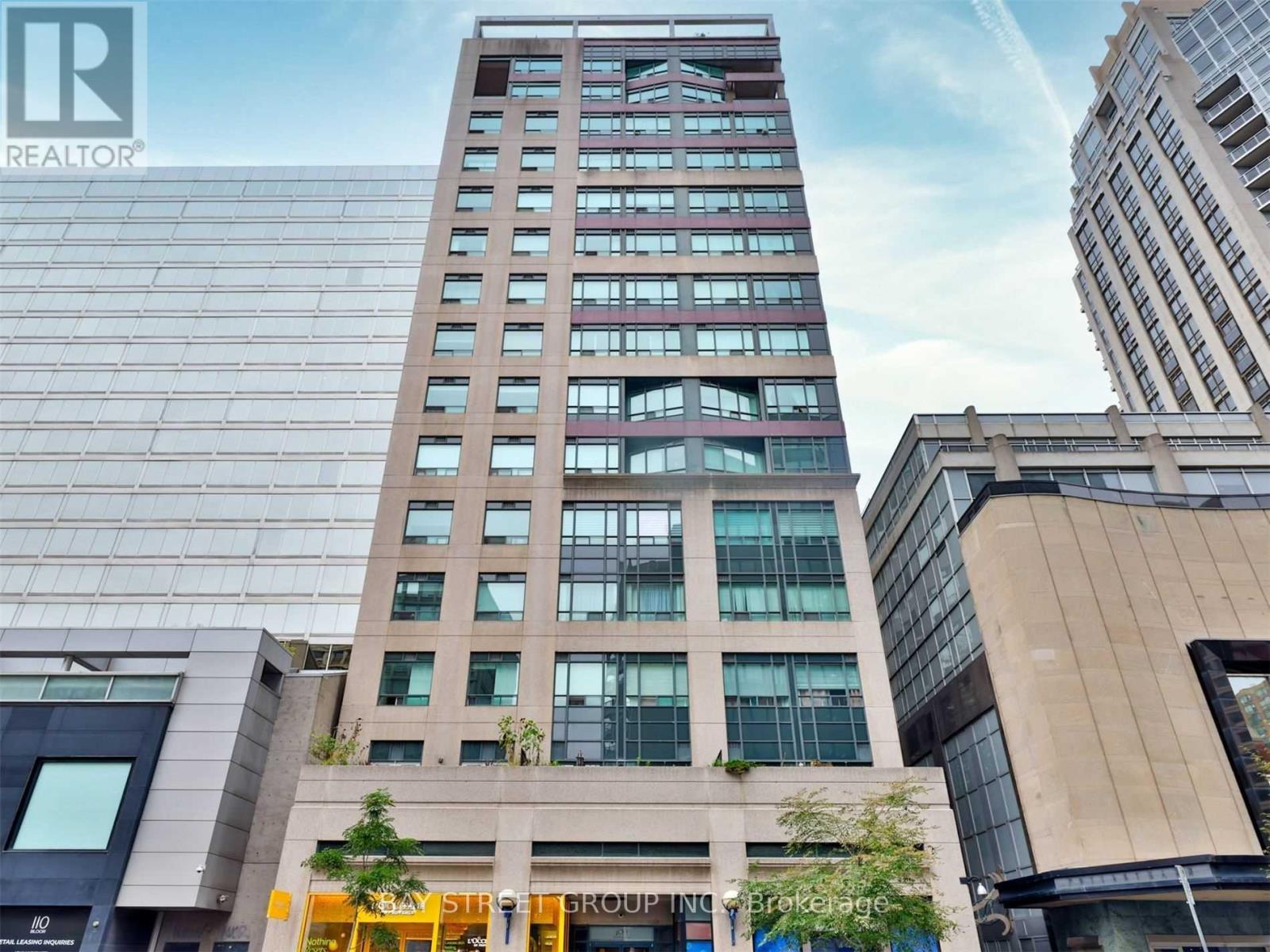A tall building with a glass facade stands in front of other buildings.